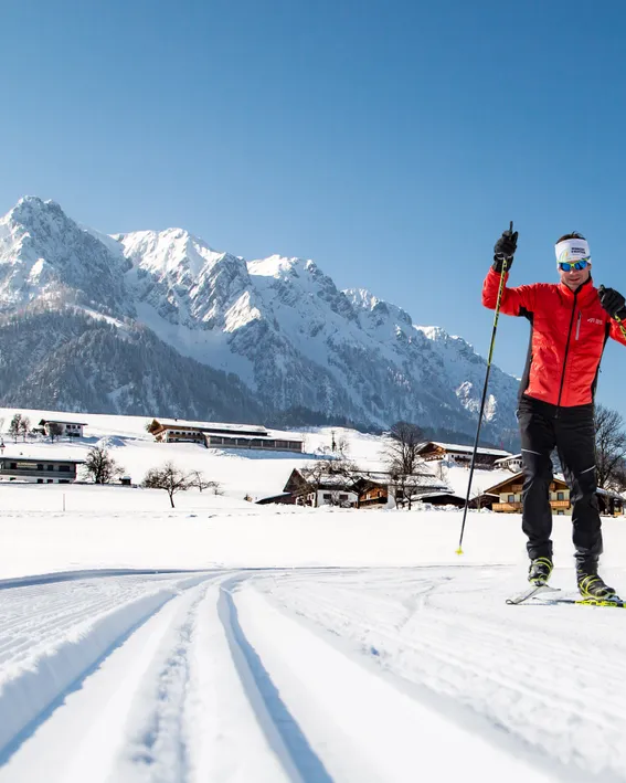 Langläufer in roter Jacke auf Loipenspur im verschneiten Alpendorf